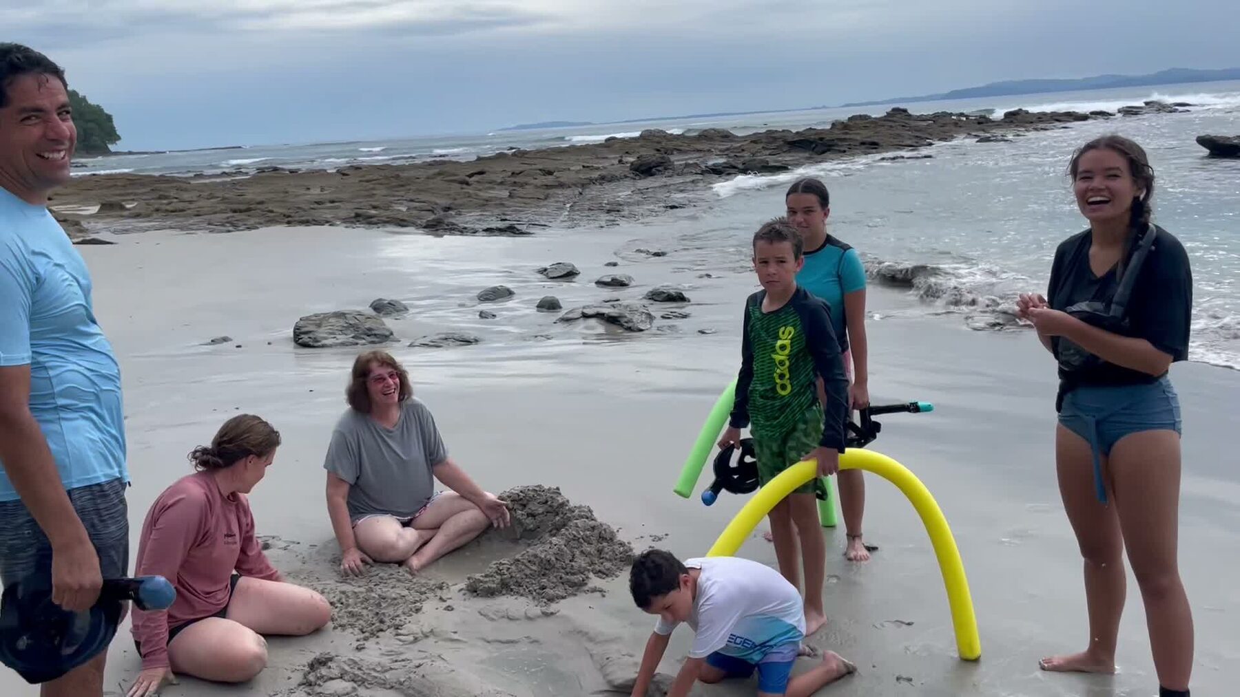 A family with kids playing on the sand with pool noodles at Playa Mantas on a best snorkel tour Jaco beach day