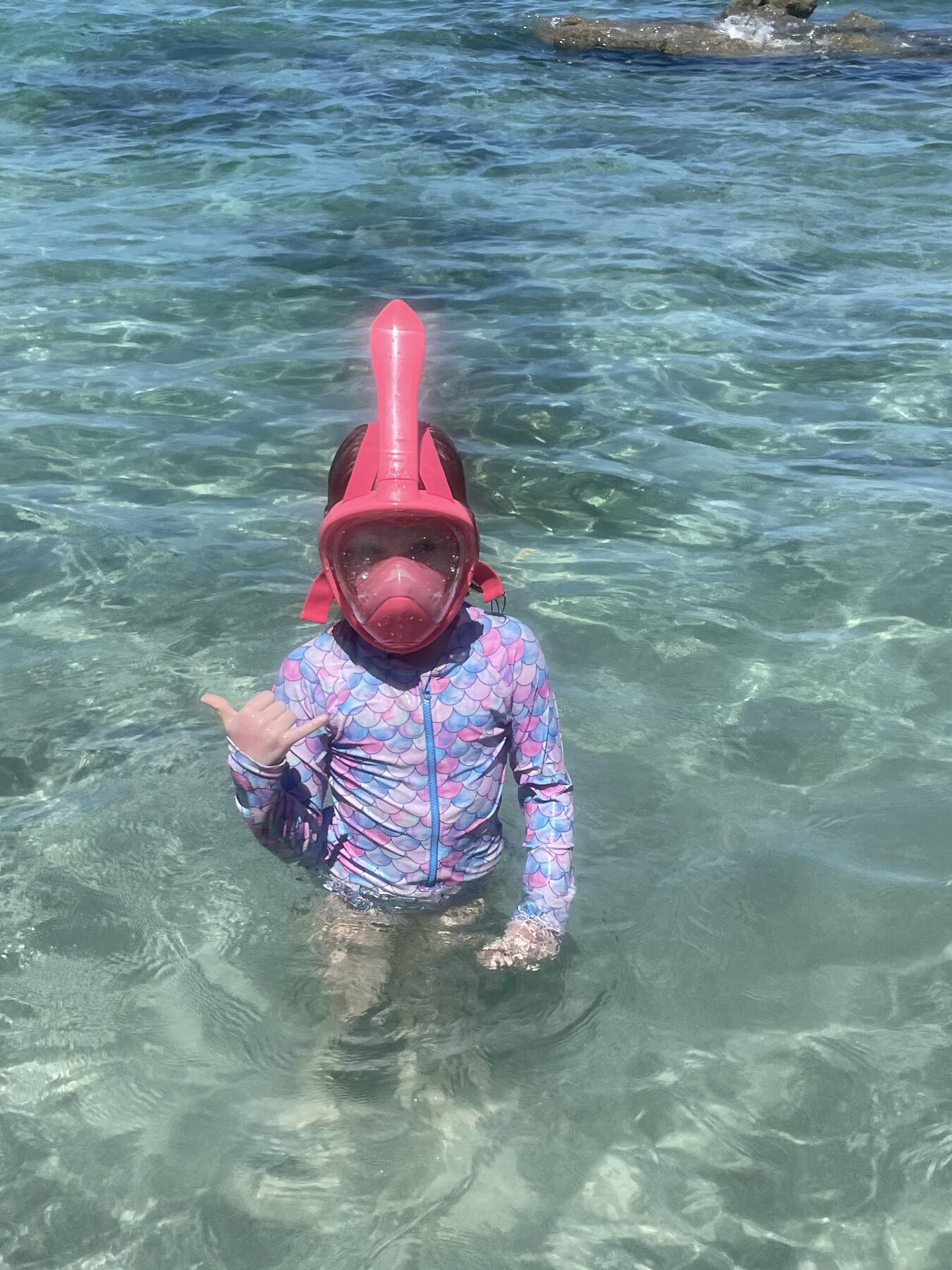 A child in a pink full-face snorkel mask in the clear water at Playa Mantas near Jacó, Costa Rica